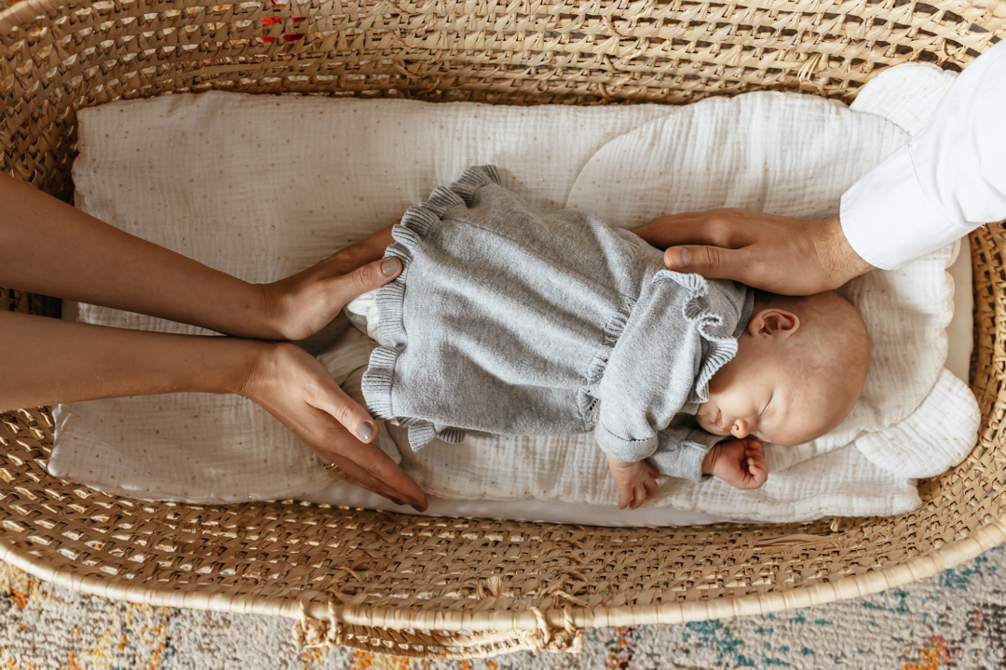 Sleeping newborn girl in a Moses basket, gently surrounded by her parents’ hands during a warm lifestyle newborn session in Abu Dhabi.