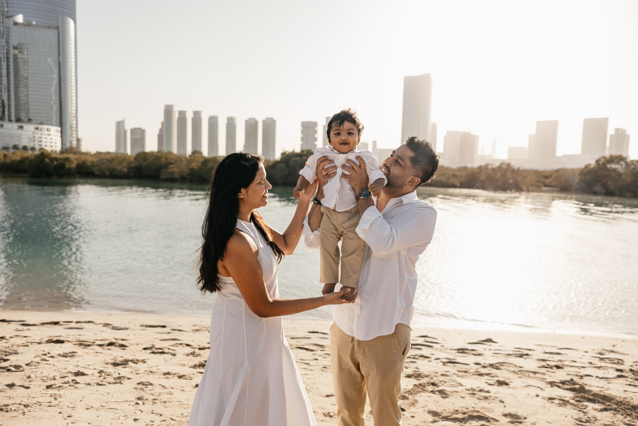 Parents lifting their one-year-old and looking at him with affection during a warm birthday beach session on Reem Island in Abu Dhabi.